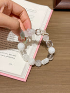 Hand holding snowfall starfield natural crystal bracelet of white phantom quartz and white agate beads with crystal cubes over an open book on a wooden table