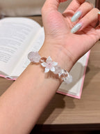 Close-up of snowfall starfield natural crystal bracelet with mother-of-pearl flower charm worn on a wrist with an open book in the background