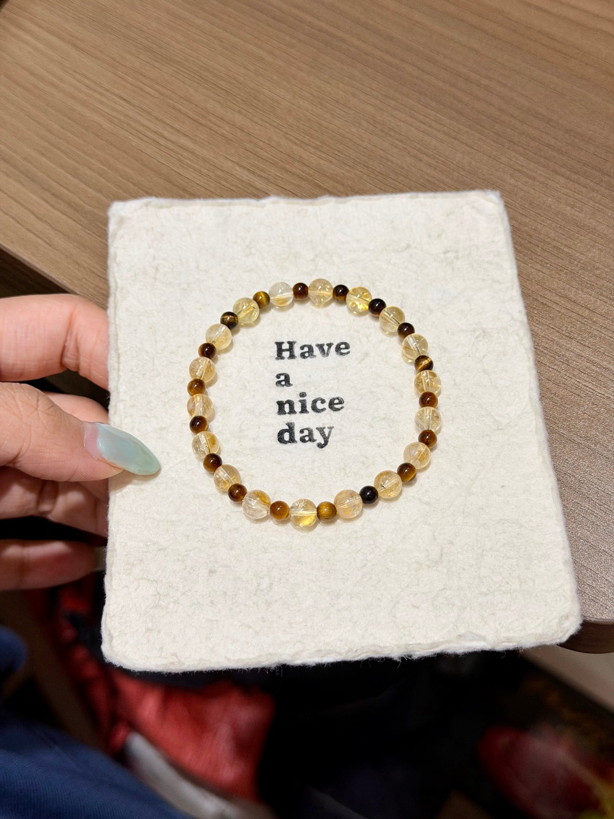 Golden brown shimmer natural crystal bracelet with yellow tiger's eye and amber beads in a circle on a Have a nice day card held in hand