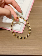Golden brown shimmer natural crystal bracelet of yellow tiger's eye and amber beads held in hand over an open book on a wooden table