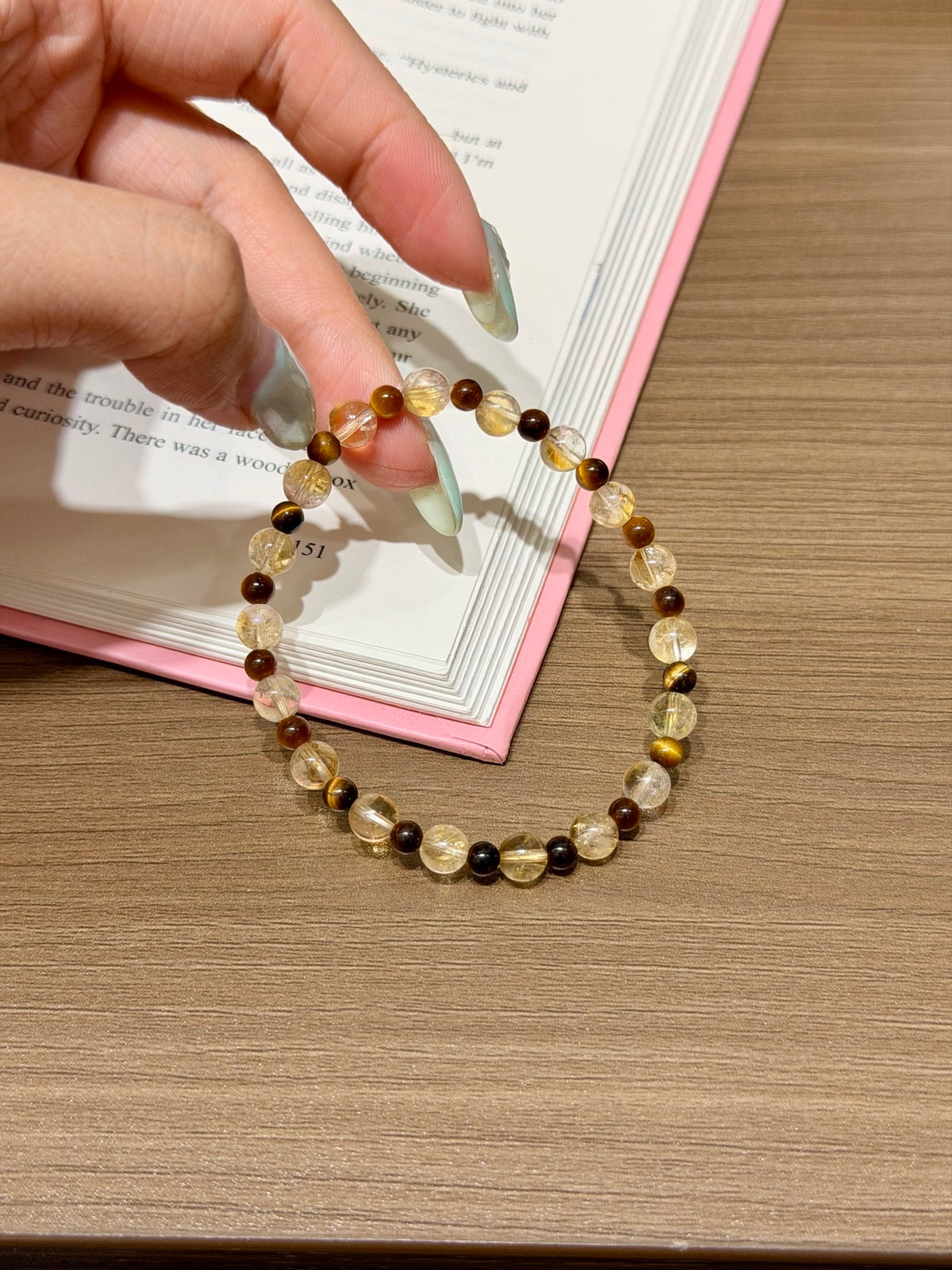 Golden brown shimmer natural crystal bracelet of yellow tiger's eye and amber beads held in hand over an open book on a wooden table