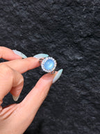 Oval aquamarine cabochon halo ring held between fingers, close-up