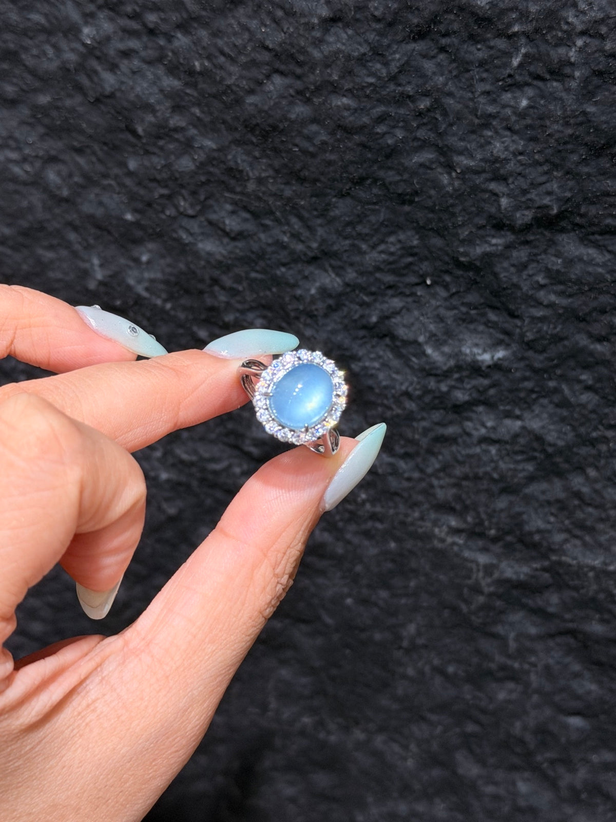 Oval aquamarine cabochon halo ring held between fingers, close-up