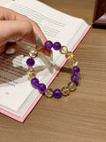Purple and gold prologue natural crystal bracelet with amethyst and citrine beads held in hand over an open book