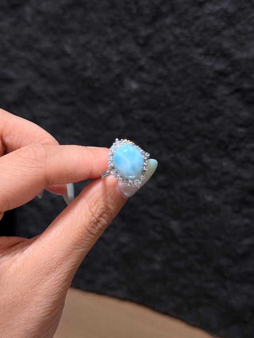 Oval larimar cabochon halo ring held between fingers, close-up