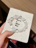 Snowfall starfield natural crystal bracelet with white phantom quartz and white agate beads in a circle on a beige card held in hand