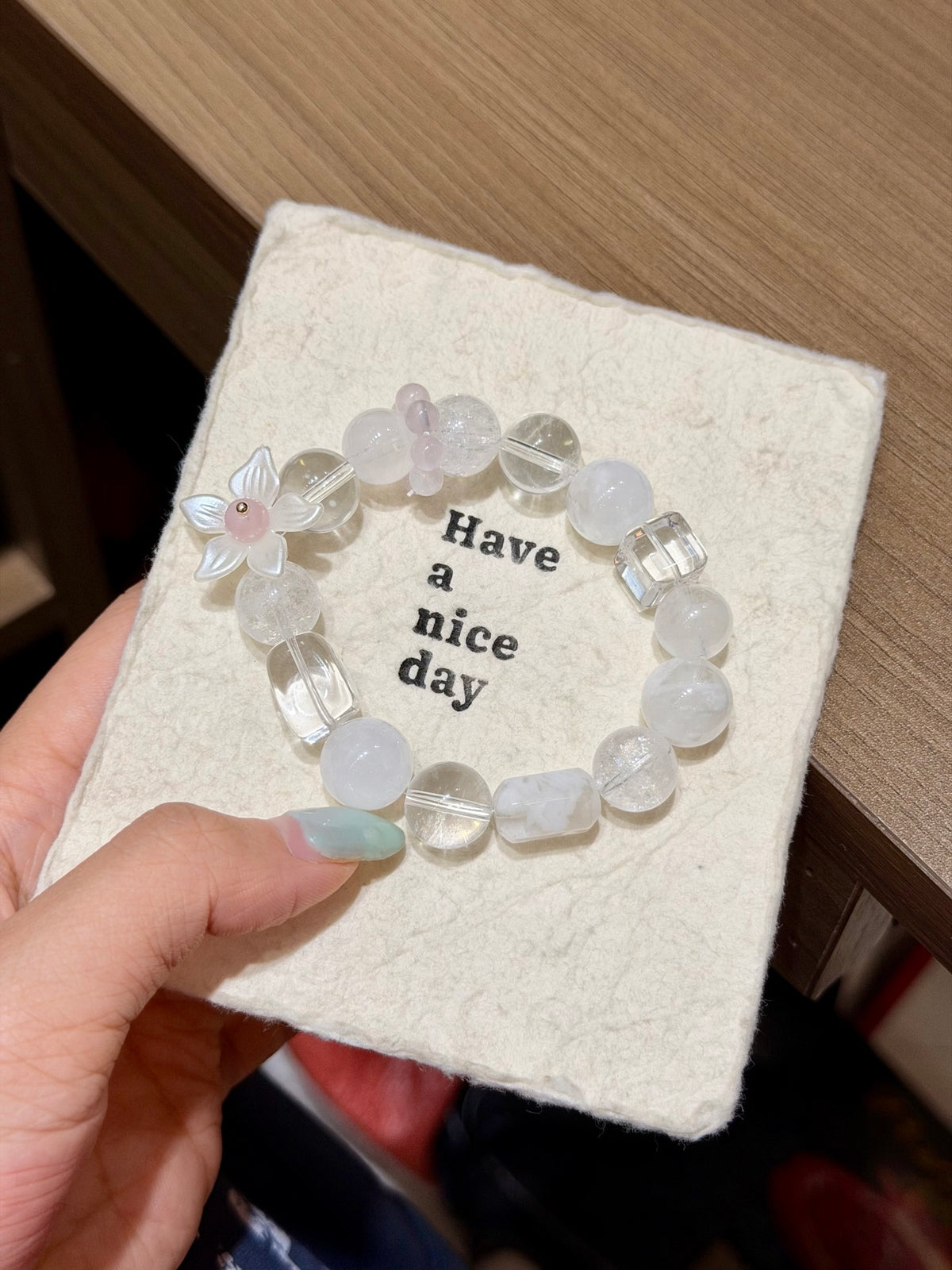 Snowfall starfield natural crystal bracelet with white phantom quartz and white agate beads in a circle on a beige card held in hand