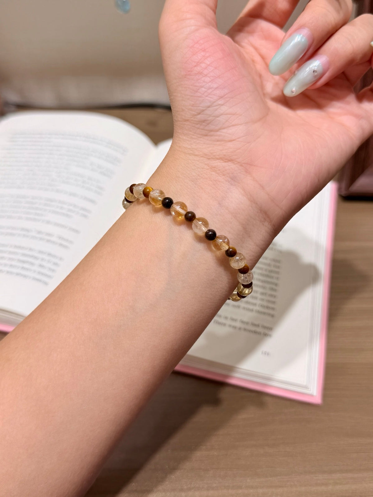 Golden brown shimmer natural crystal bracelet with yellow tiger's eye beads worn on a wrist with an open book in the background