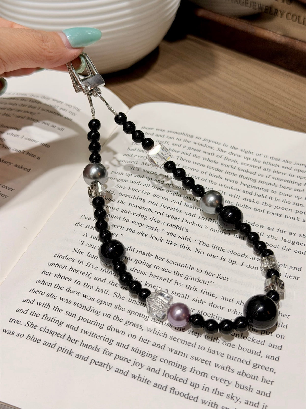 Black obsidian and pearl bag charm with metal clasp on an open book