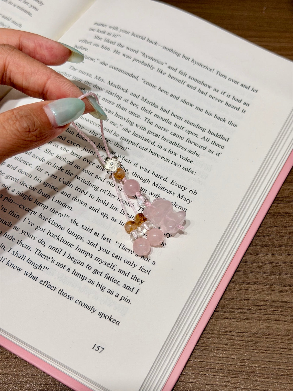 Pink quartz bear phone charm with pink cord on an open book