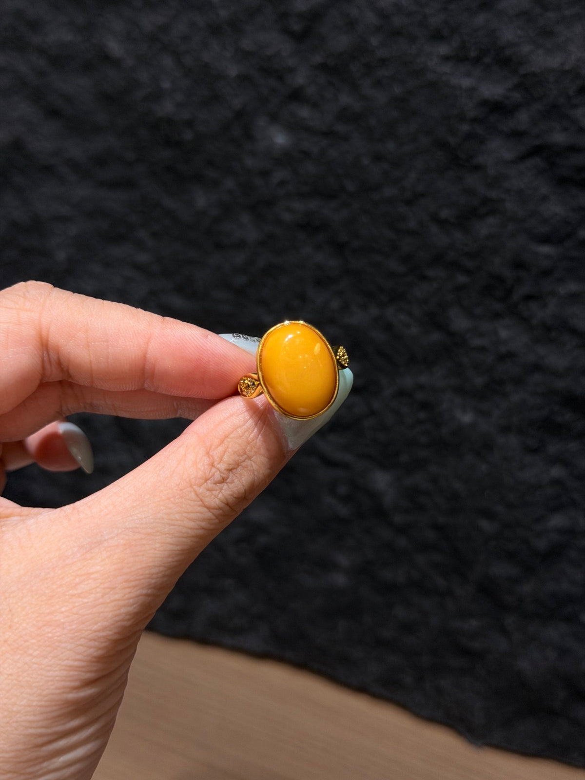 Honey amber solitaire ring with 18K gold plated setting held between fingers