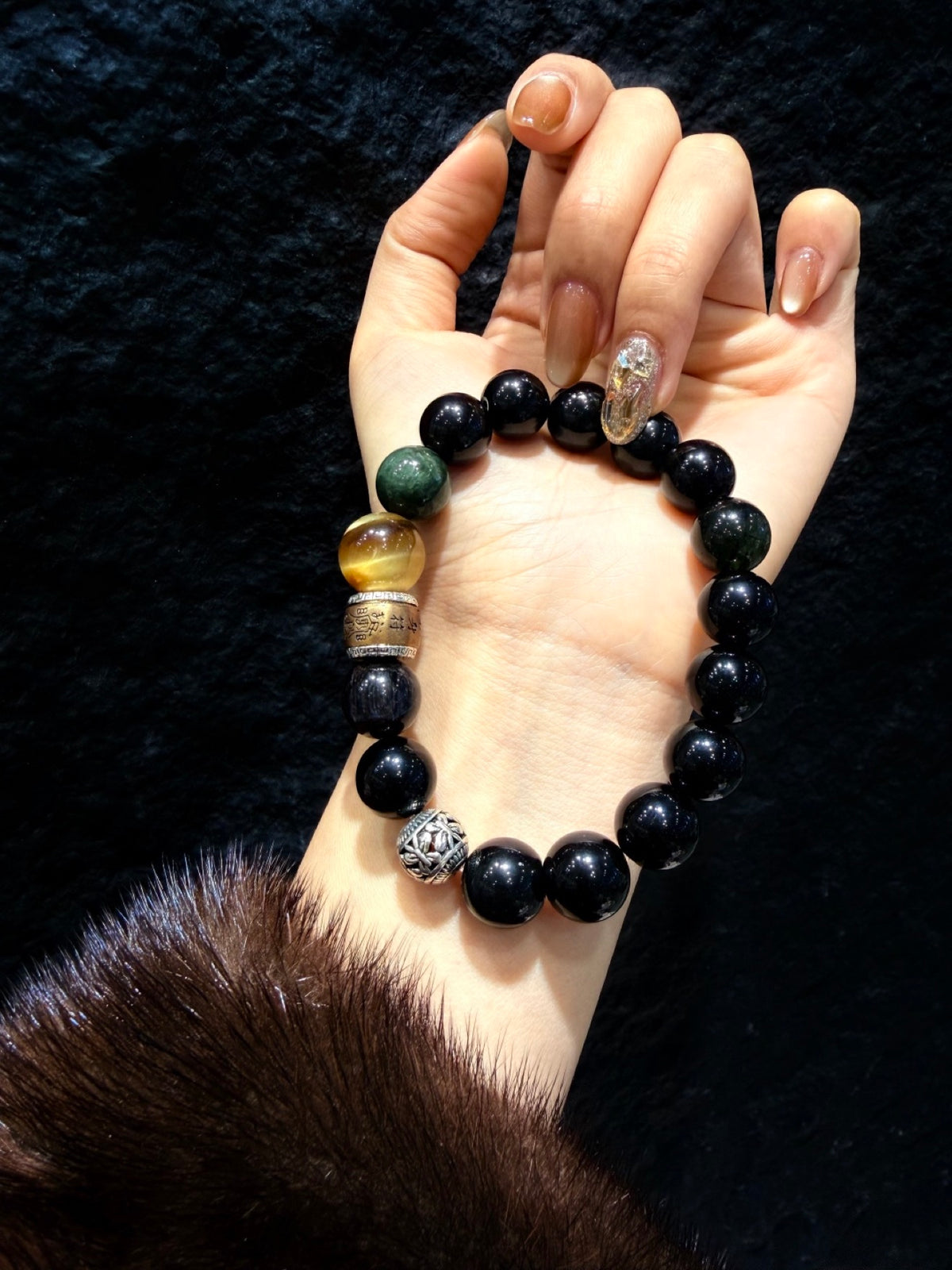 Obsidian Guardian Bracelet on wrist against dark background, golden tiger's eye and green rutilated quartz beads
