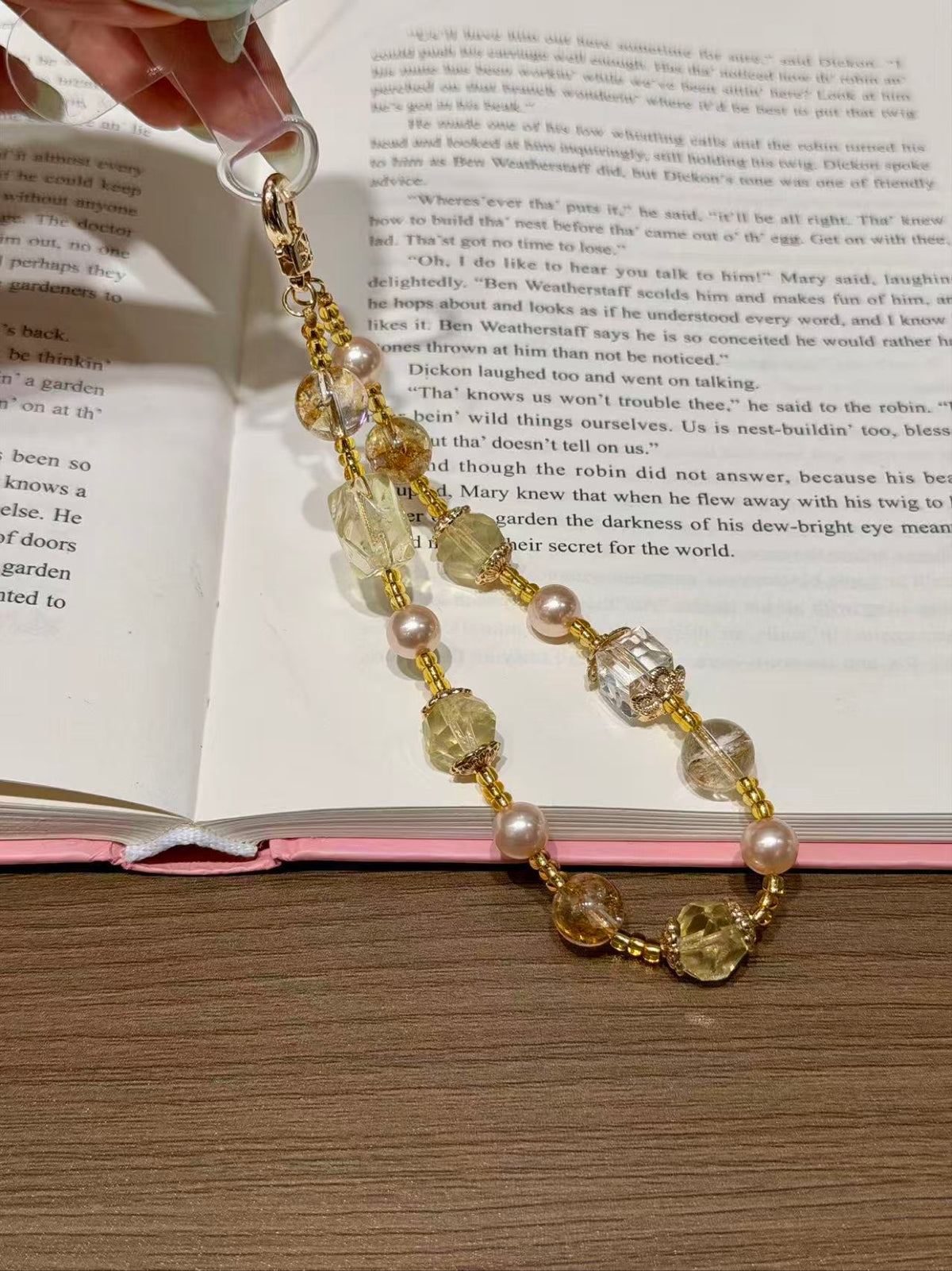 Gold and citrine crystal phone charm with shell beads on an open book