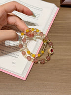 Honeyberry Gilt Bracelet held over an open book, showing pink strawberry quartz and yellow citrine beads