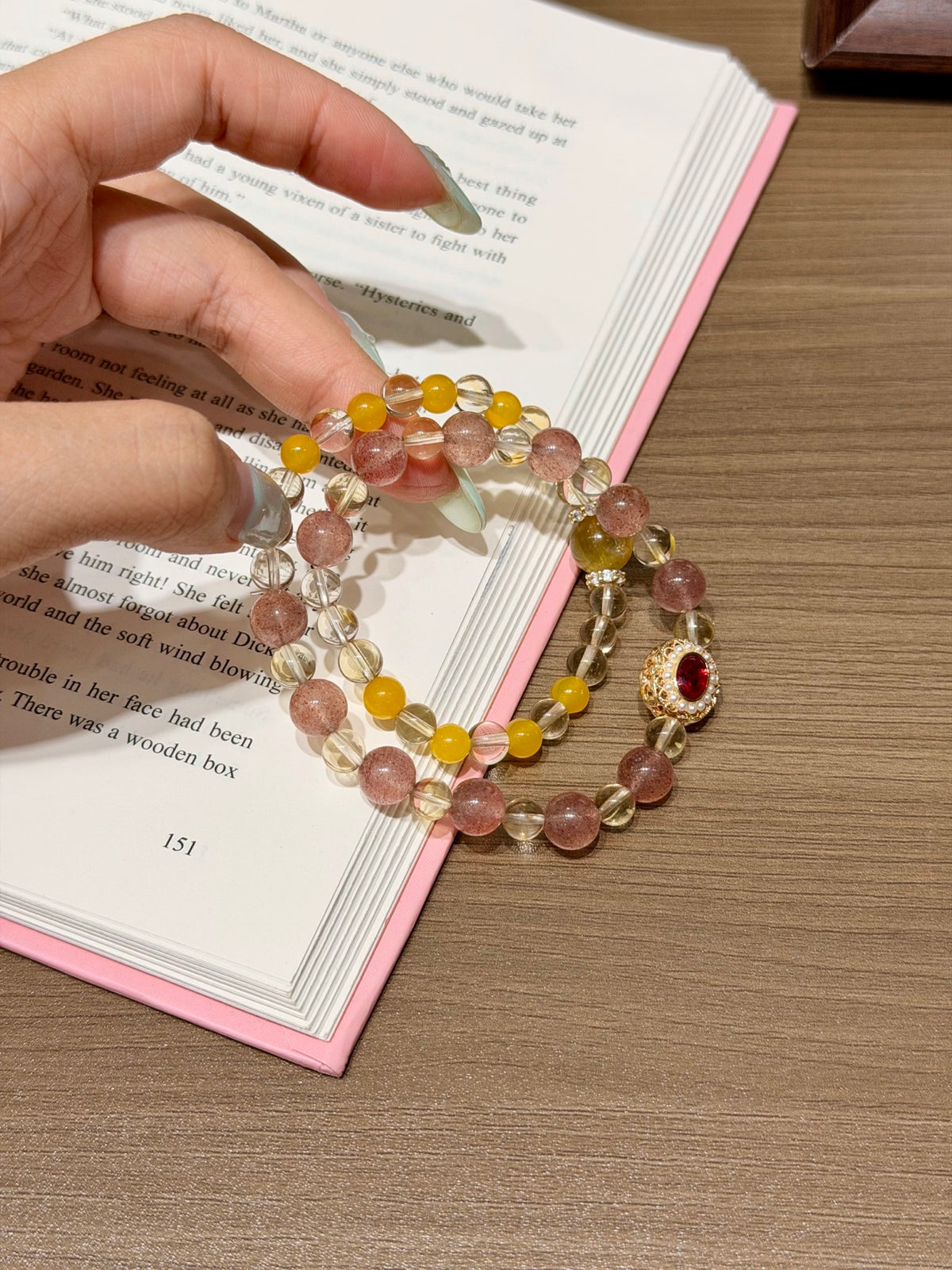 Honeyberry Gilt Bracelet held over an open book, showing pink strawberry quartz and yellow citrine beads